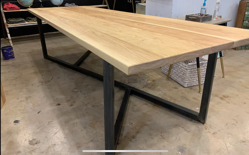 A long ash dining table with a black steel base in the workshop