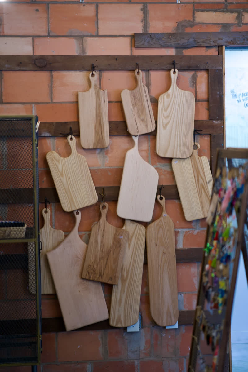 Handmade serving boards hung in rows against a brick wall in the shop