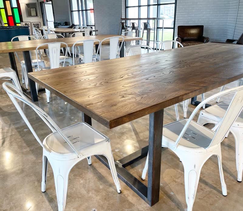 A long oak communal table with a steel base and white metal chairs