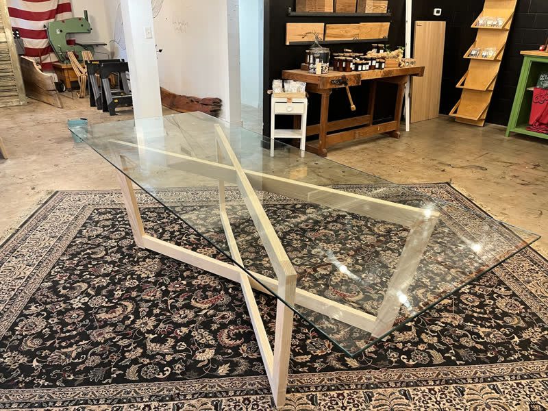 A glass-top dining table on a hand-built ash cross base in the Mercy Goods shop
