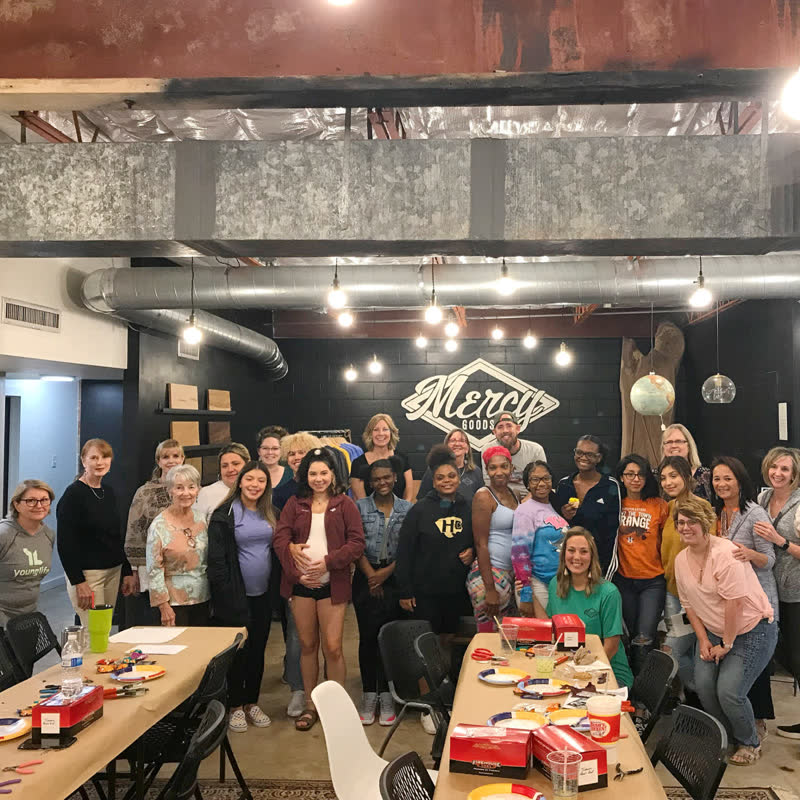 A full room of volunteers and students gathered beneath the Mercy Goods sign during a community event