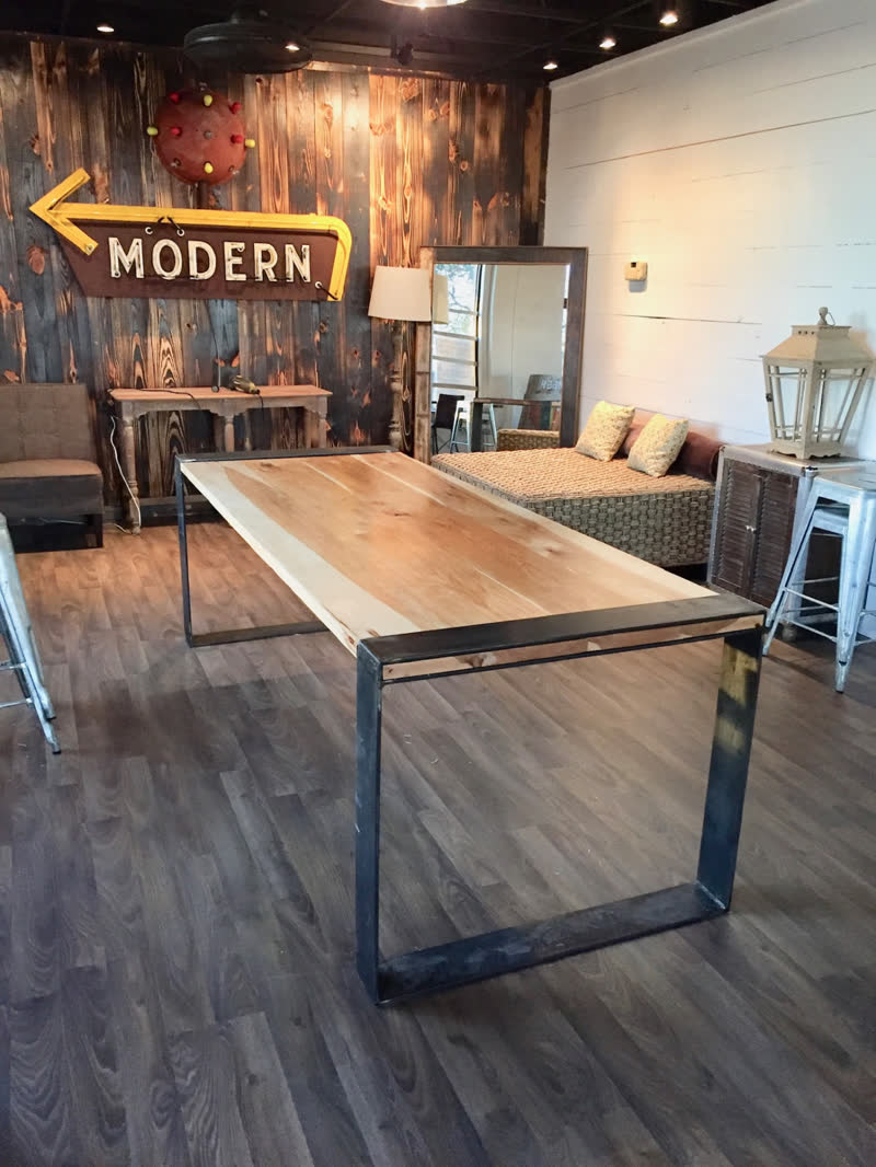 A live-edge slab table with a thick black steel box base on the showroom floor