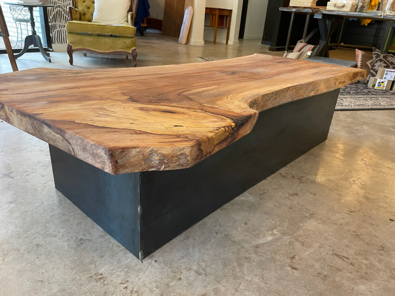 A thick live-edge coffee table on a blackened steel box base in the showroom
