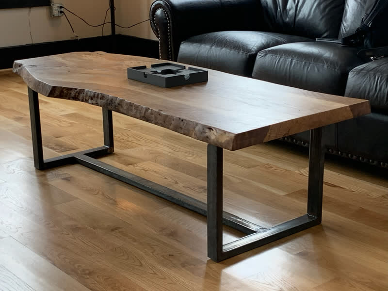 A live-edge coffee table on a steel frame in front of a leather sofa