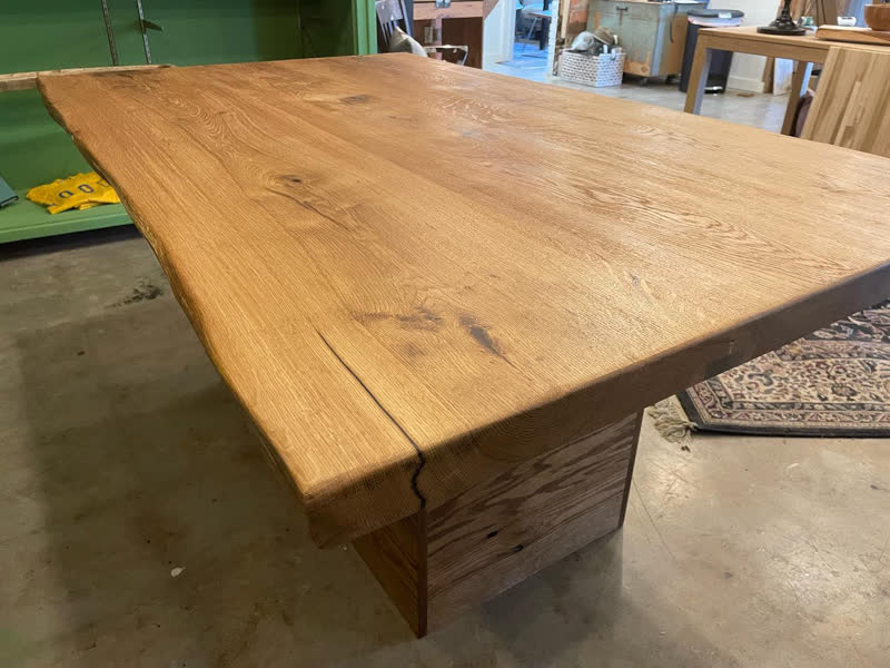 A thick live-edge oak tabletop on a wooden base, fresh in the shop