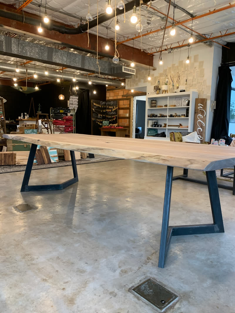A long live-edge table on angled steel legs under the shop's hanging lights