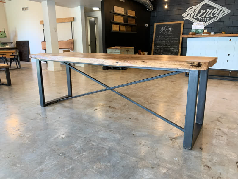 A long live-edge table with X-braced black steel legs in the Mercy Goods shop