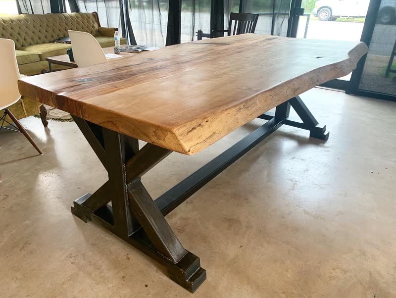 A large live-edge table on a black X-frame steel base, delivered to a client's office
