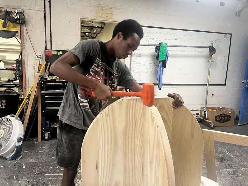A young maker tapping a curved cabinet piece together with a mallet