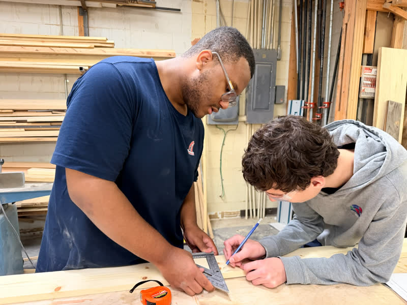 Two young makers measuring and marking a board with a speed square and pencil