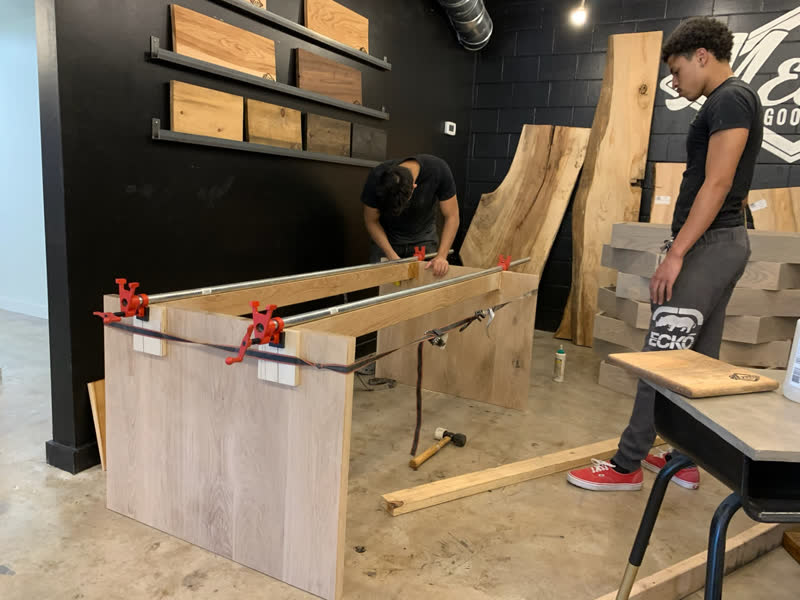 Two young makers gluing and clamping an oak table base with pipe clamps