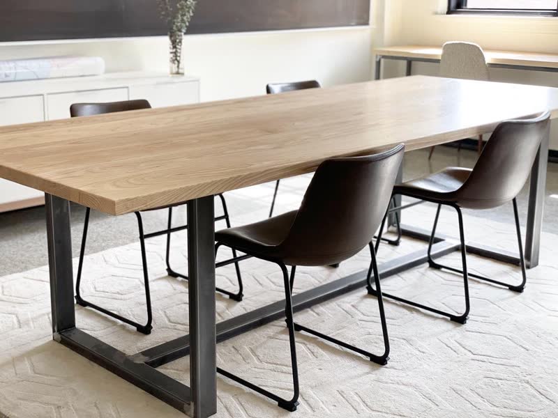 A light oak dining table with a black steel base and leather chairs