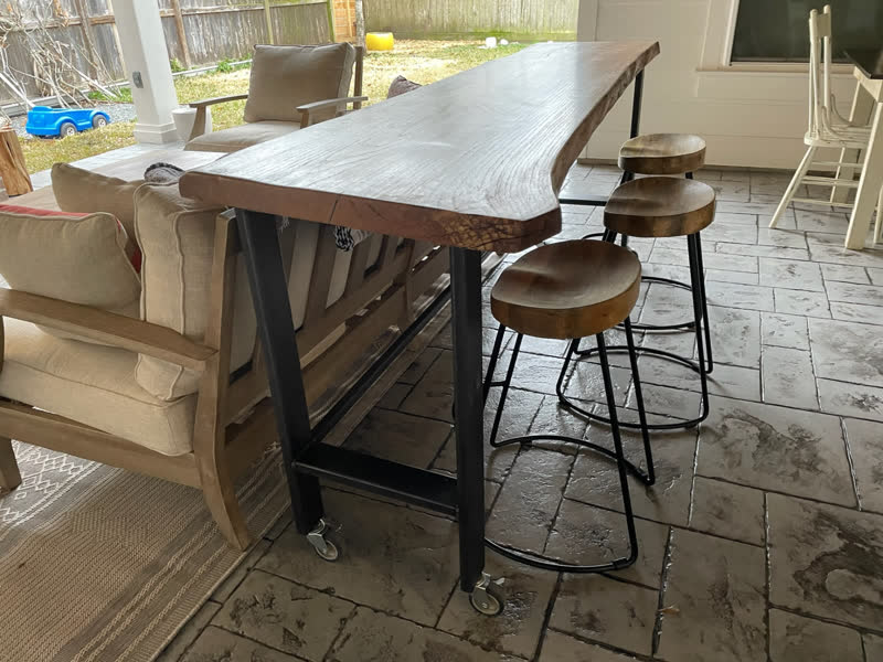 A live-edge bar table on casters with wooden stools, on a covered patio