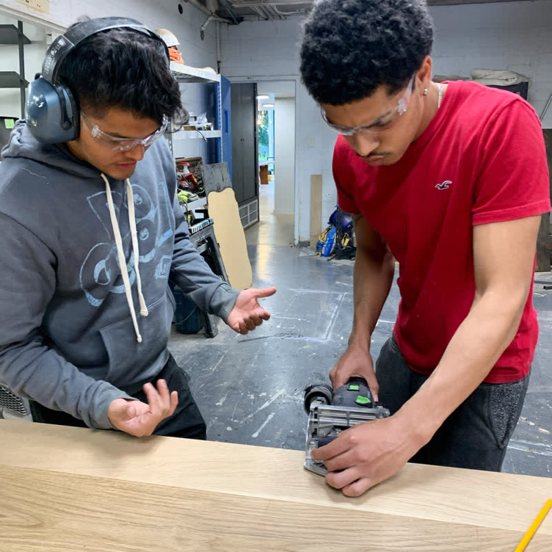 One young maker guiding another through a cut with a plate joiner