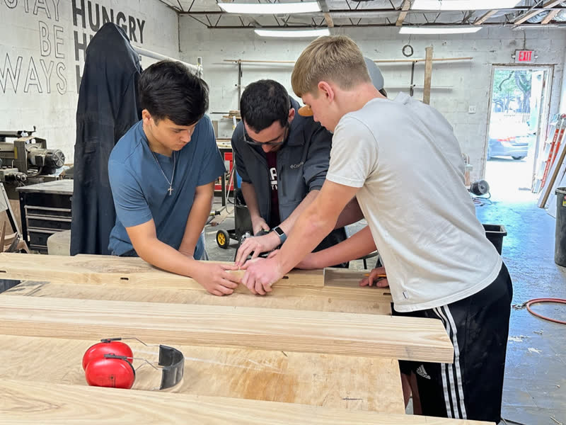 Three makers fitting pocket-hole rails together on a tabletop in the workshop