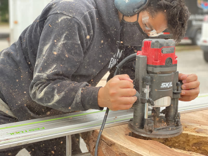A young maker routing a live-edge slab, wood chips flying
