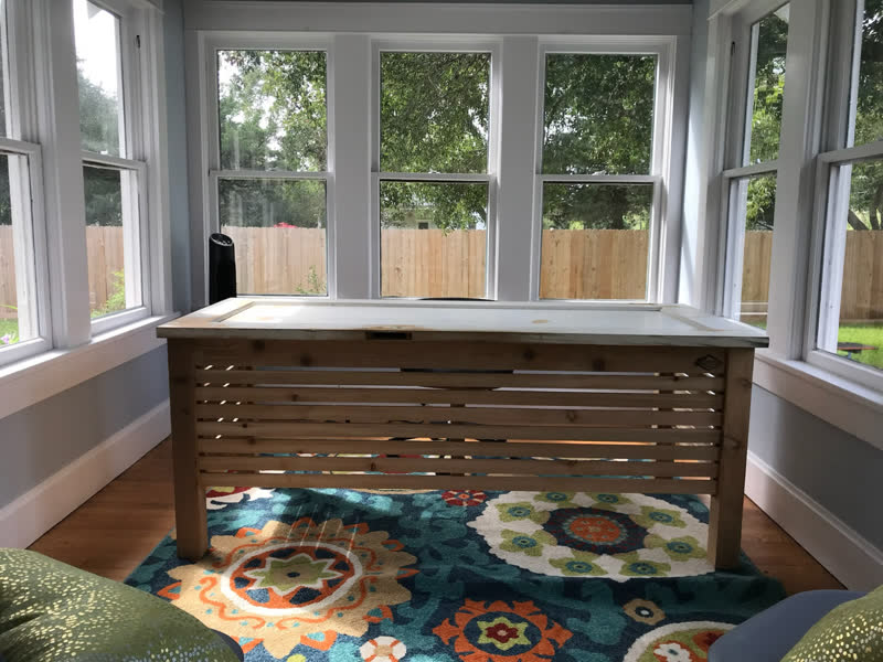 A slatted-front desk with a salvaged window for its top, in a bright sunroom