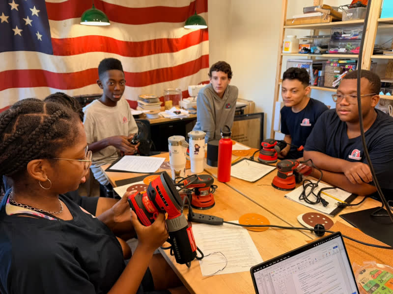 A class of young makers learning to use orbital sanders around the work table