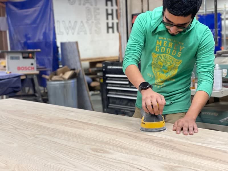 A student sanding a tabletop smooth in the Mercy Goods workshop