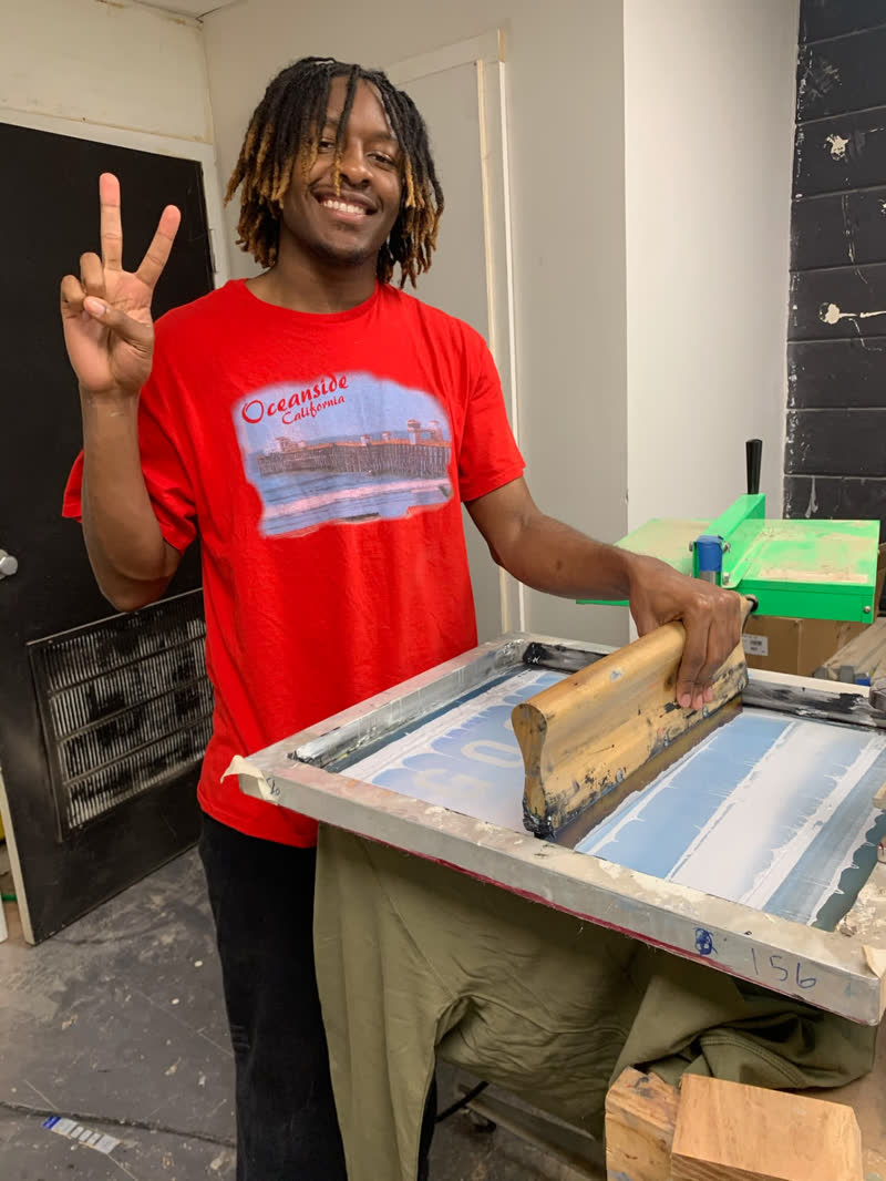 A young maker screen printing a shirt while flashing a peace sign