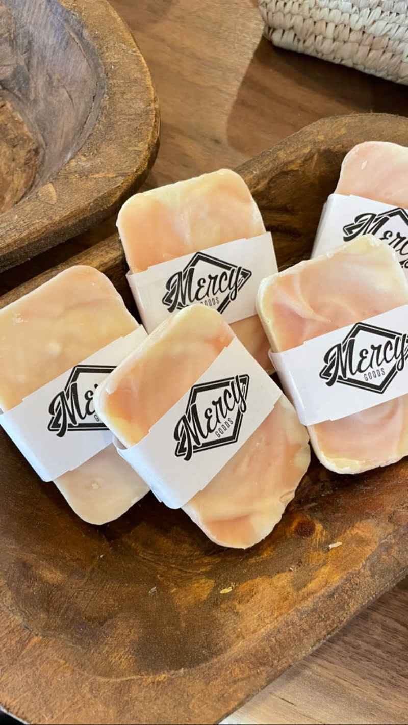 Mercy Goods handmade soaps wrapped in branded bands, in a carved wooden bowl
