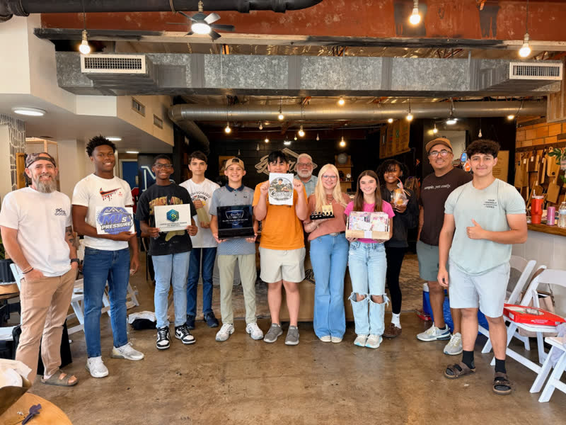A group of teen entrepreneurs holding up their business projects in the Mercy Goods shop