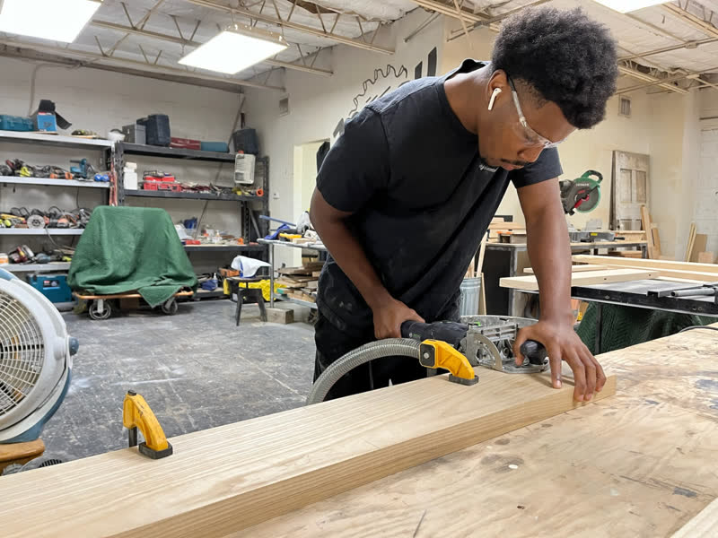 A young maker in safety glasses making a clean cut along a clamped board