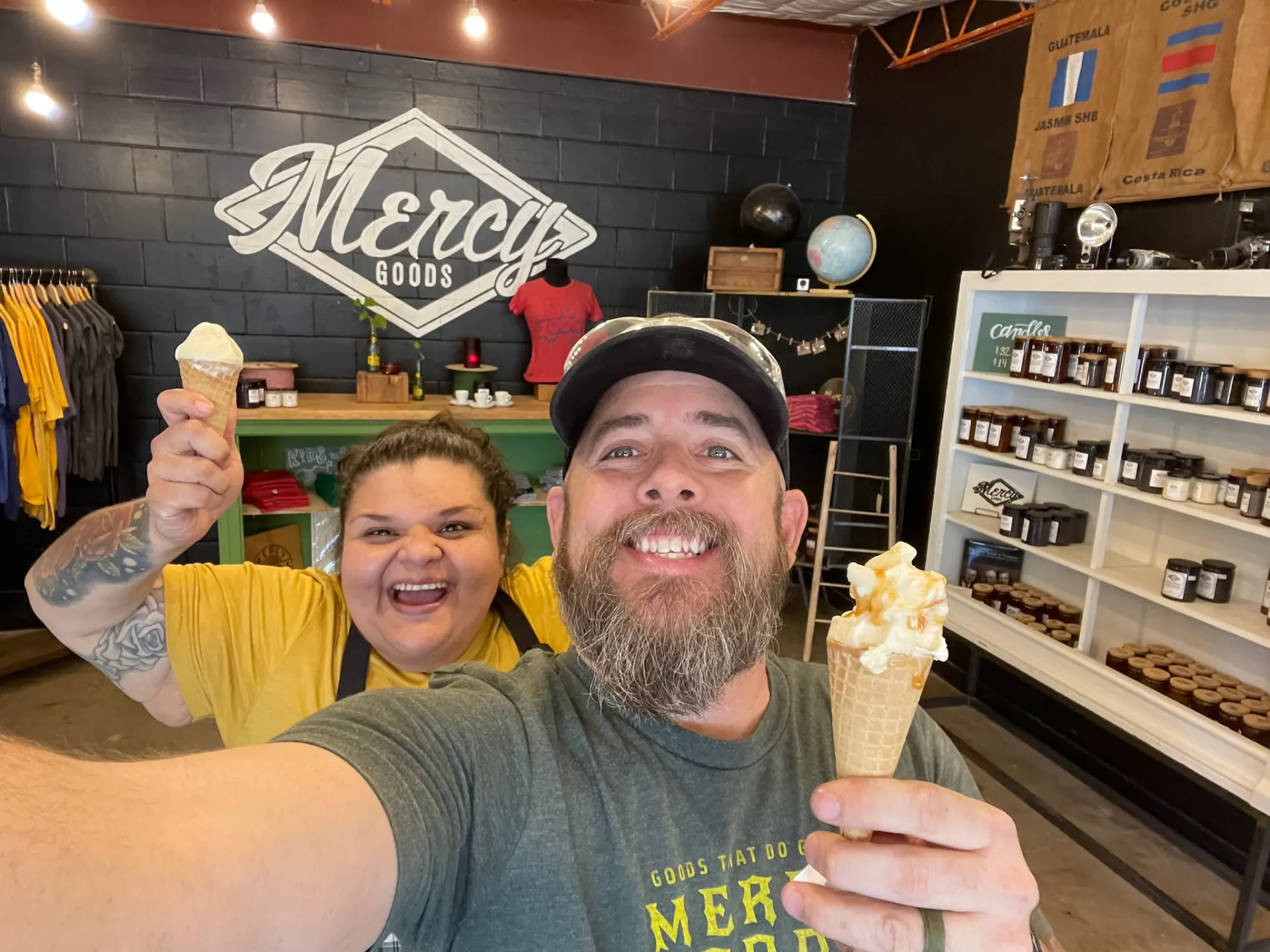 Two smiling Mercy Goods team members celebrating with ice cream cones beneath the Mercy Goods mural