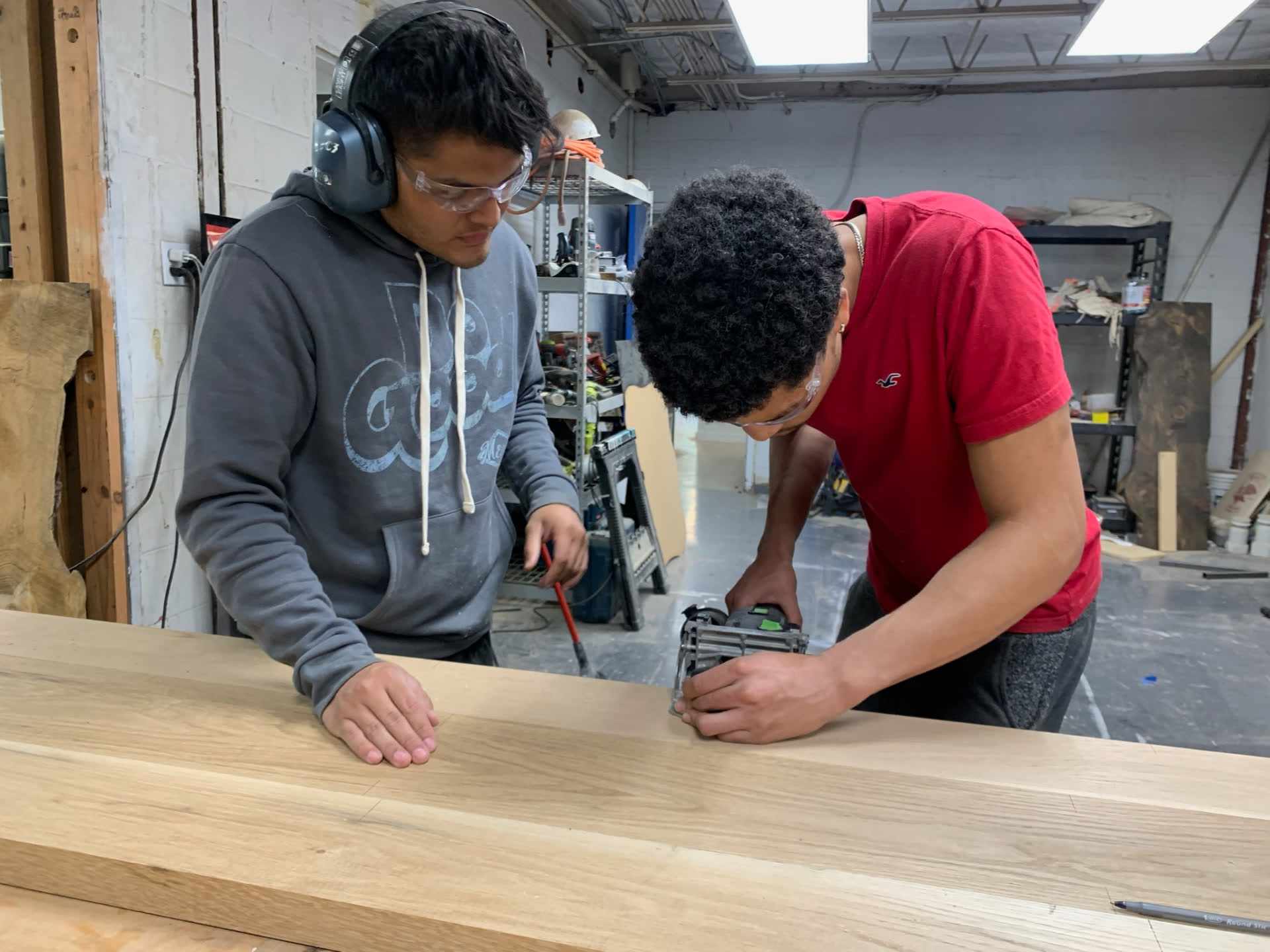 Two students cutting a board together in the Mercy Goods workshop