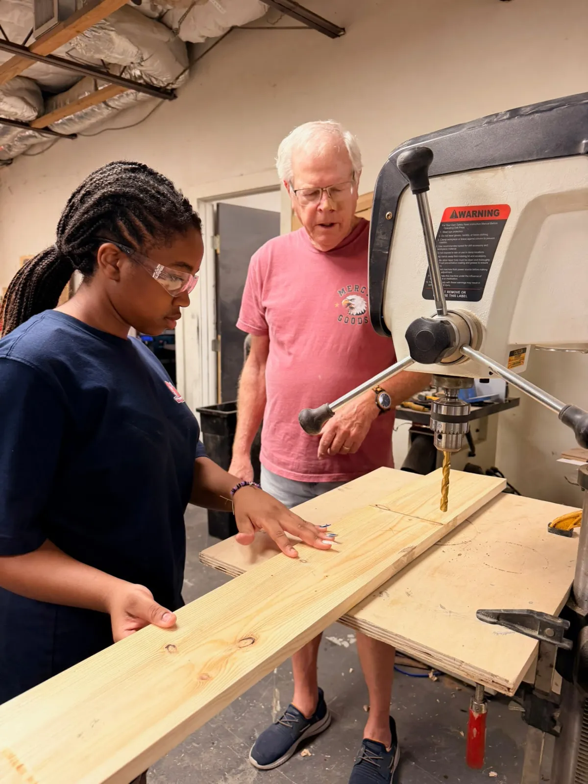 A mentor guiding a young woman at the drill press at Mercy Goods